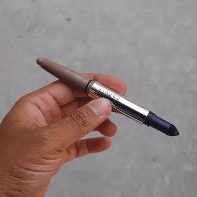 Silver dual-ended Clinique eyeshadow stick with grey and dark blue ends exposed