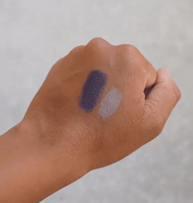The back of a hand with navy blue and grey eyeshadow swatches