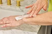 A person applies Acure Seriously Soothing 24hr Moisture Lotion to their forearm