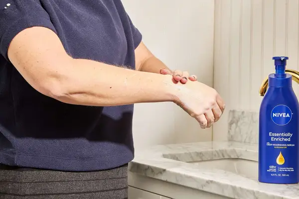 person rubbing Nivea Essentially Enriched Hand and Body Lotion on back of and and arm