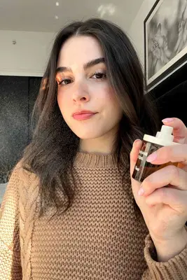 Person holding perfume alongside fragrances for teens from PHLUR, Replica, and Snif displayed on a counter
