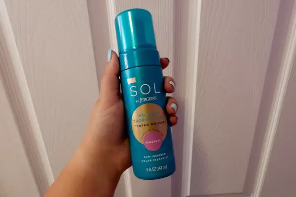 Hand holding Sol by Jergens No Wait Tropical Tan Tinted Mousse self-tanner