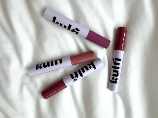 Four Kulfi Beauty Lip Oils against white sheet backdrop