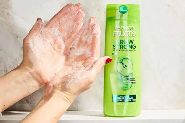 A person lathering the Garnier Fructis Grow Strong Shampoo onto their hands