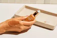 Hand holding a bottle of Flower Beauty Get Real Serum Foundation with foundation on the back of their hand