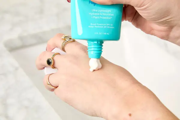 A person applying COOLA Classic Body Organic Sunscreen Lotion to the back of their hand
